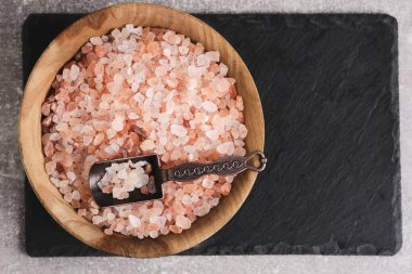 Ahşap bardakta pembe Himalaya tuzu ve kayrak zeminde bir baharat kaşığı.