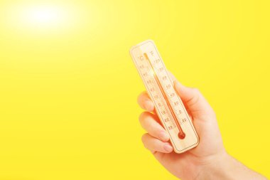 Elindeki termometre 30 derecelik ısıyı gösteriyor. Parlak sarı arkaplan