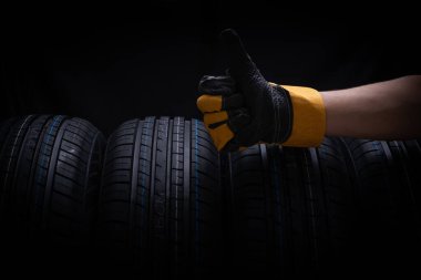 Hand in gloves with car tires on black background, close-up clipart