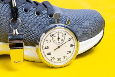 Spor ayakkabılar, ıslık ve kronometre sarı arka planda. Zaman yönetimi kavramı