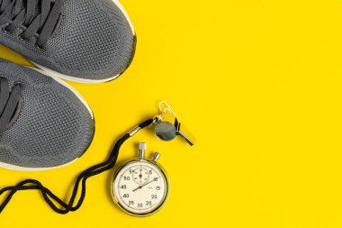 Spor malzemeleri: Spor ayakkabıları, kronometre ve sarı arka planda ıslık. Yukarıdan görüntüle