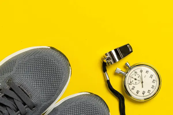 Spor malzemeleri. Sarı arka planda spor ayakkabılar, ıslık ve kronometre