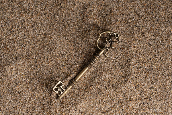 Vintage key on the sand background. Top view. Copy space