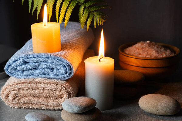 Spa still life with towels, sea salt and burning candles on a background of fern foliage