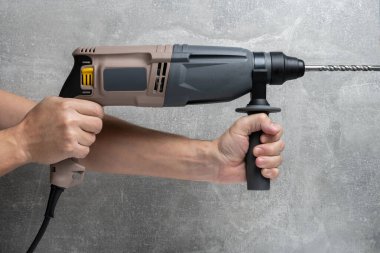 Arka plandaki beton duvara karşı elektrikli bir delgi tutan insanların büyük bir görüntüsü.