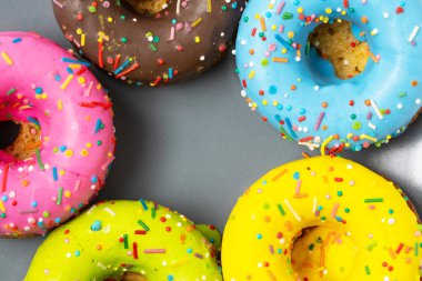 Colorful donuts with sprinkles on grey background, top view clipart