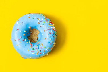 Blue glazed donut with sprinkles on yellow background, top view clipart