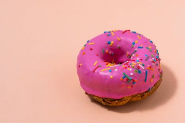 Pembe kremalı çörek ve pembe arka planda renkli serpiştirmeler.