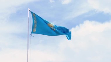Kazakistan bayrağı rüzgarda dalgalanıyor arkadaki beyaz bulutlara ve mavi gökyüzüne.