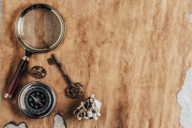 Antika anahtar, pusula, büyüteç ve arka plandaki eski kağıt.