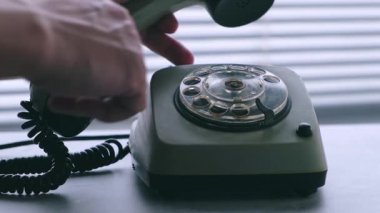 Eski bir telefonun alıcısını elle kaldırır ve çevirerek numarayı çevirir. Perdeleri kapalı bir pencerenin arka planına karşı. Yakın çekim..