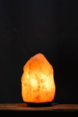 Siyah arka planda, ahşap masada güzel aydınlatılmış tuz lambası.