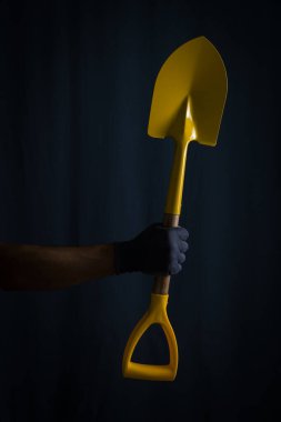 Eldivenli adam sarı küreği koyu arka planda tutuyor.