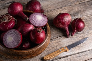 Ahşap arka planda tahta kasede kırmızı soğan ve bıçak.