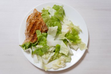 Beyaz mutfak masasında yeşil salata ve barbekü eti. Çin lahanası, salata yaprakları, ızgara kazık. Sağlıklı yemek, temiz yeme konsepti. Üst görüntü. Yüksek kalite fotoğraf