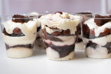 Cream and biscuit layered dessert. Homemade chocolate, vanilla cream and cherry trifles in transparent glasses, variation of dessert on white table. High quality photo clipart