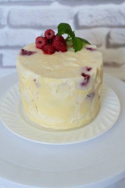 Beyaz çikolatayla kaplanmış ve kırmızı yay ahududuyla süslenmiş ev yapımı kek, yeşil nane yaprağı kusurlu pişirme, evdeki pasta sulu sulu pasta ve beyaz tabakta taze böğürtlen.