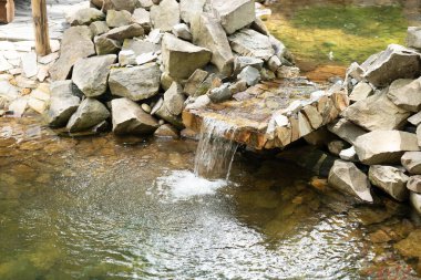 Temiz su, pürüzsüz taşların üzerine düşer. Etrafı kayalarla çevrili sakin bir havuzda dalgalanmalar yaratır. Gün ışığında doğanın barışçıl atmosferini yansıtır. Yüksek kalite fotoğraf