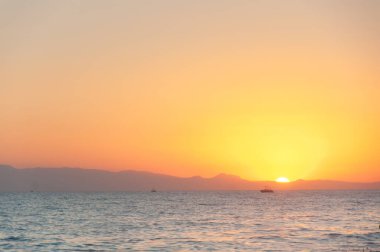 Deniz sahilinde harika bir gün batımı manzarası. Sakin su dalgaları, turuncu gökyüzündeki tepeler. Rahatla, akşamları meditasyon. Yüksek kalite fotoğraf