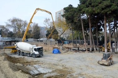 Beton bir pompa kolu çimentoyu uzun bir çitin üzerine döküyor. Park alanında inşaat