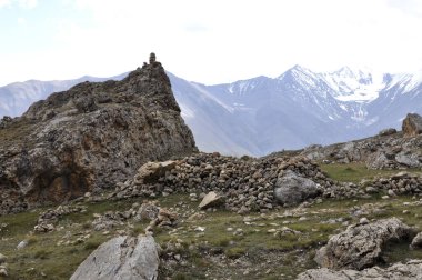 Yolcuların, çobanların ve turistlerin yollarını bulmalarına yardım etmek için dağın eteklerinde taş bir kule. Karlı dağların eteğindeki yosunlu taşlardan yapılmış bir kule. Arkaplan veya dergi için yüksek kaliteli doğa görüntüsü