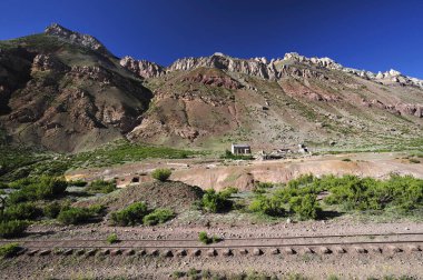 Bir demiryolu hattının kenarındaki dağlık arazide yalnız bir ev. Gök gürleyen, kayalık bir dağın eteğinde terk edilmiş harap olmuş bir taş ev..