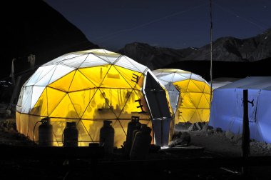 Dağların arasında bir keşif gezisi tarafından kurulan sarı çadır. Kamp alanı. Turizm sezonu. Gecenin karanlığında içinde ışıklar olan bir kamp. Kamp sezonu
