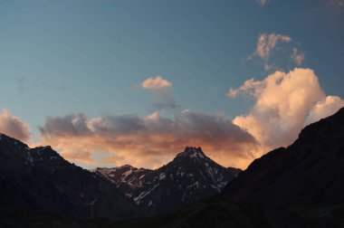 Gün batımında bulutlu karlı dağlar. Bulutlar ve gökyüzü güneş batarken muhteşem bir altın renge dönüyor. Dağ turizmi için mükemmel bir seçim..