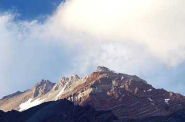 Gün batımında bulutlu karlı dağlar. Bulutlar ve gökyüzü güneş batarken muhteşem bir altın renge dönüyor. Dağ turizmi için mükemmel bir seçim..