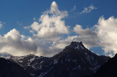 Gün batımında bulutlu karlı dağlar. Bulutlar ve gökyüzü güneş batarken muhteşem bir altın renge dönüyor. Dağ turizmi için mükemmel bir seçim..