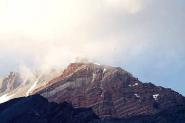 Gün batımında bulutlu karlı dağlar. Bulutlar ve gökyüzü güneş batarken muhteşem bir altın renge dönüyor. Dağ turizmi için mükemmel bir seçim..