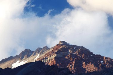 Gün batımında bulutlu karlı dağlar. Bulutlar ve gökyüzü güneş batarken muhteşem bir altın renge dönüyor. Dağ turizmi için mükemmel bir seçim..