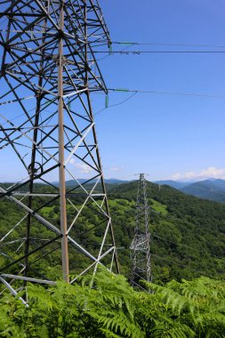 Mavi gökyüzü ve dağların arkasında elektrik iletim hatları var. Elektrik..