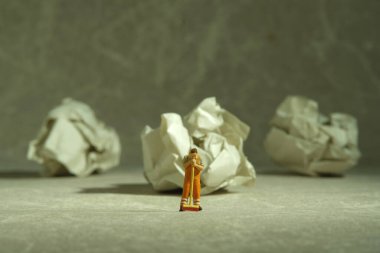 Miniature people toy figure photography. Tired sweeper standing in front of crumple ball of paper on the floor. Image photo clipart