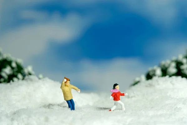 Miniature people toy figure photography. Winter holiday. Kids brother and sister playing snowball throwing. Image photo