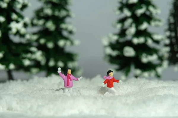 Miniature people toy figure photography. Winter holiday. Kids brother and sister playing snowball throwing in the pine fir forest. Image photo