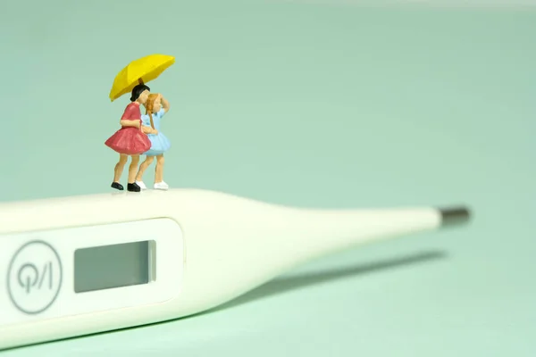 Miniature people toy figure photography. Two girls kid standing above white thermometer. Isolated on green background. Image photo