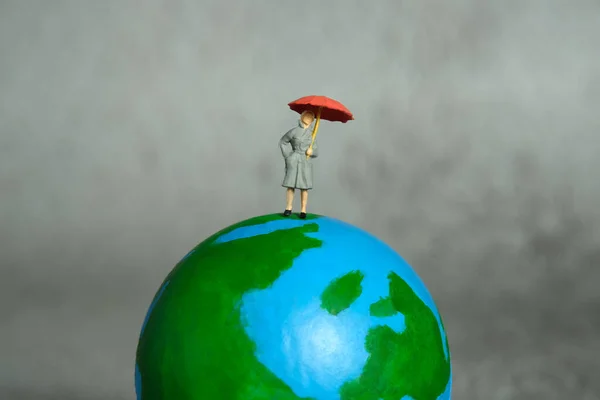 Miniature people toy figure photography. Women news presenter standing above earth globe presenting weather forecast. Grey cloudy background. Image photo