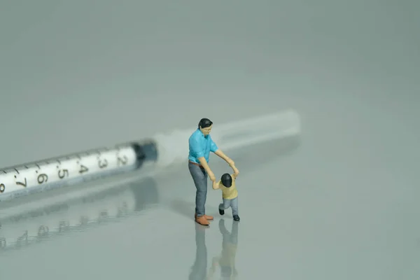 Miniature people toy figure photography. Refusing for injection concept. A father and son standing in front of needle syringe on grey background. Image photo