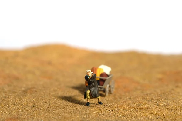 Miniature people toy figure photography. An old woman grandma walking alone, moving in the middle of desert, going to refugee camp because of war conflict. Image photo