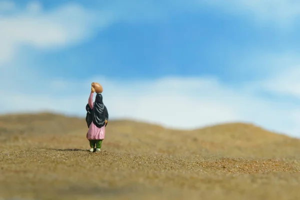 Miniature people toy figure photography. Drought issue and problem. Women wearing veil walking in the middle of dessert carrying a jug above the head. Image photo