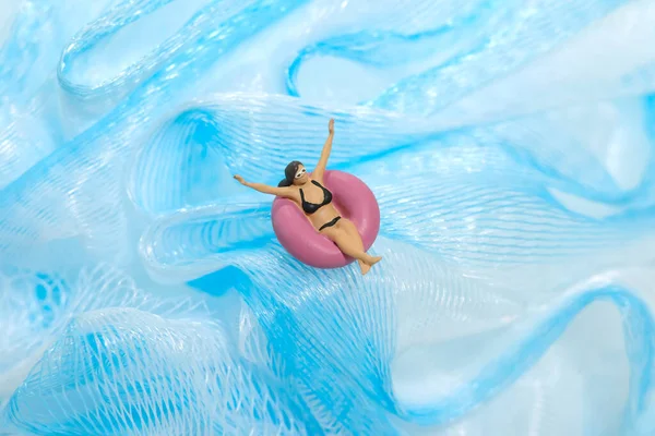 Miniature people toy figure photography. Girl wearing black sunglasses swimming with rubber tube ring on wavy ocean. Image photo