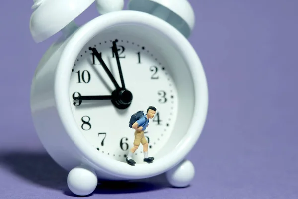微小的人物玩具摄影 一个背着背包的男生站在时钟旁边 被紫色背景隔离 图片照片 — 图库照片