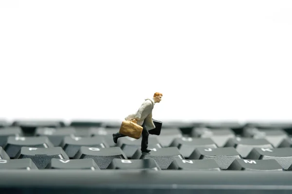 Miniature tiny people toy figure photography. A businessman running above black keyboard carrying briefcase. Isolated on white background. Image photo