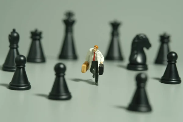 Miniature tiny people toy figure photography. A businessman running in the middle of chess pawn carrying briefcase. Isolated on grey background. Image photo