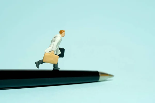 Miniature tiny people toy figure photography. A businessman running above black pen carrying briefcase. Isolated on blue background. Image photo