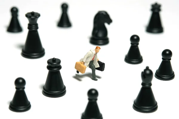 Miniature tiny people toy figure photography. A businessman running in the middle of chess pawn carrying briefcase. Isolated on white background. Image photo