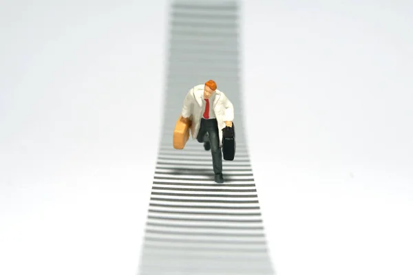 Miniature tiny people toy figure photography. A man wearing white coat on zebra crossing at the street road. Isolated on white background. Image photo
