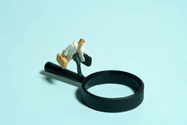Miniature tiny people toy figure photography. A man wearing with coat running above magnifier glass. Isolated on blue background. Image photo
