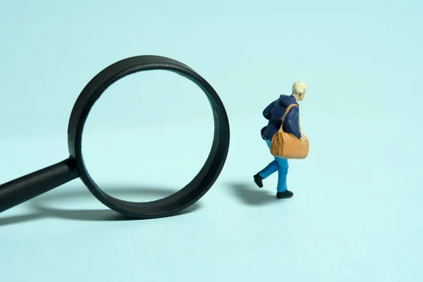 Miniature tiny people toy figure photography. A college student running in front of magnifier glass. Isolated on blue background. Image photo